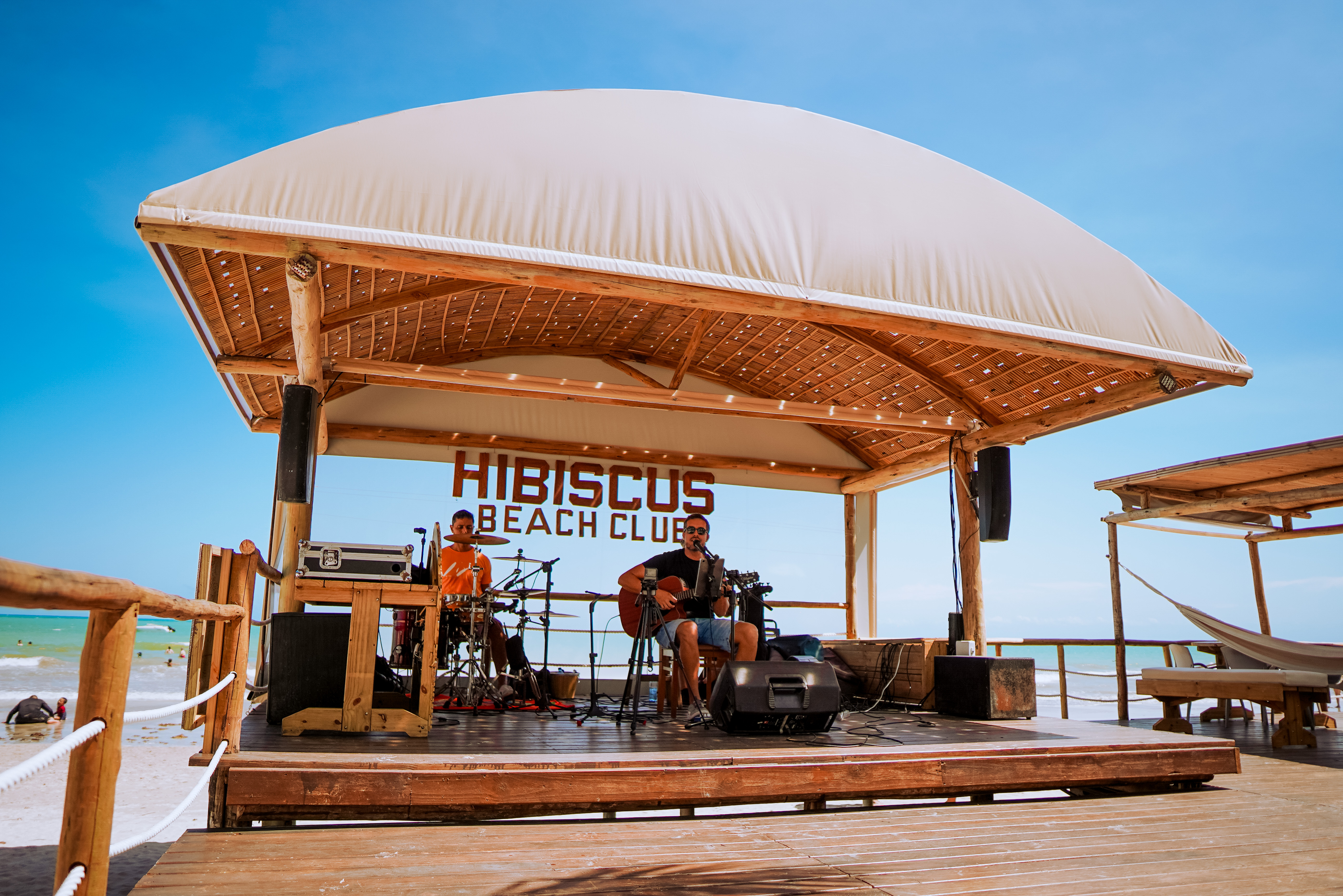 Banda ao vivo no palco do Hibiscus Beach Club com o mar atrás
